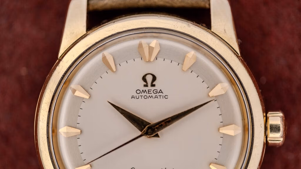 Close-up of a gold Omega Automatic wristwatch with a white dial and gold hour markers on a brown background, showcasing the timeless style linked to Omega serial numbers.