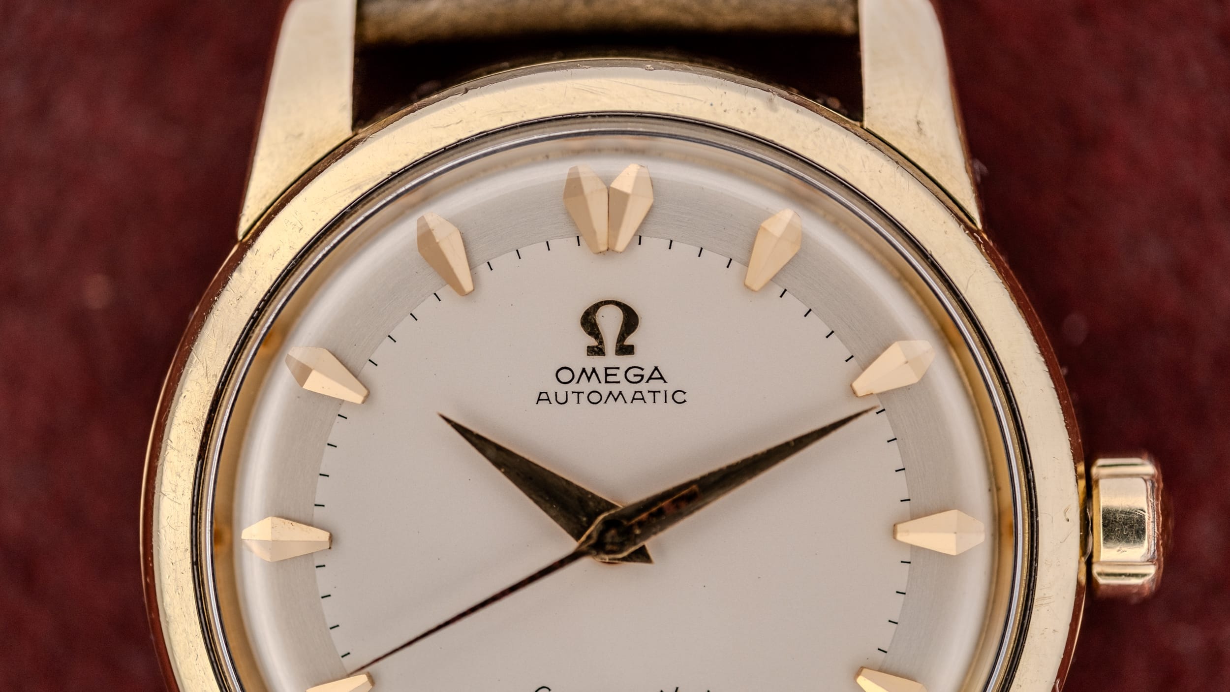 Close-up of a gold Omega Automatic wristwatch with a white dial and gold hour markers on a brown background, showcasing the timeless style linked to Omega serial numbers.