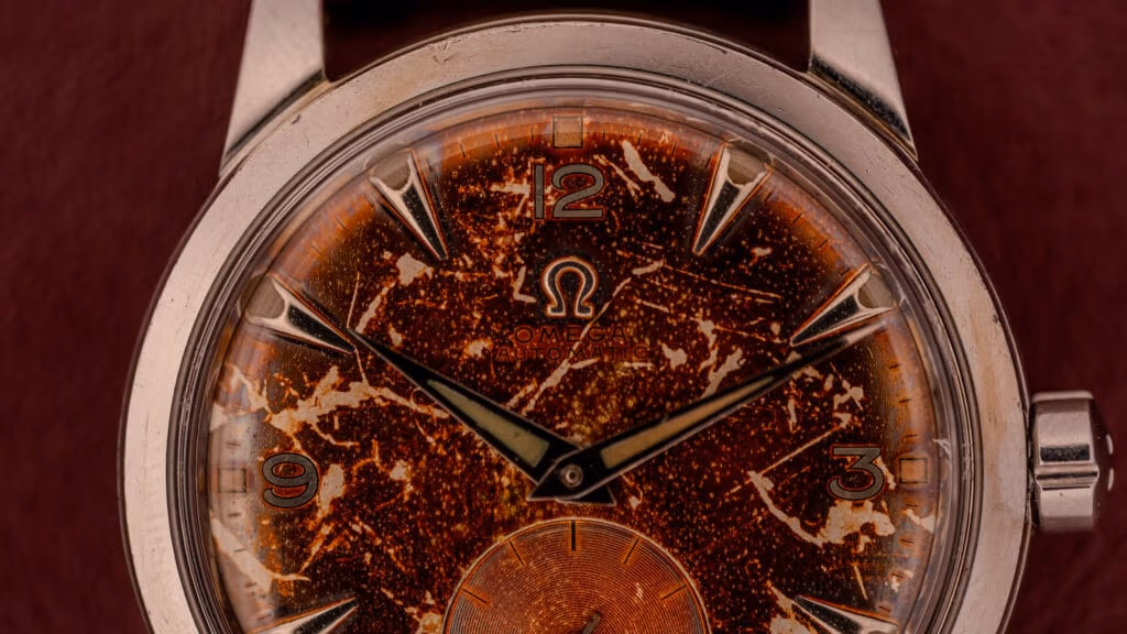 Close-up of a vintage Omega bumper watch with a weathered, speckled brown dial and silver hands.