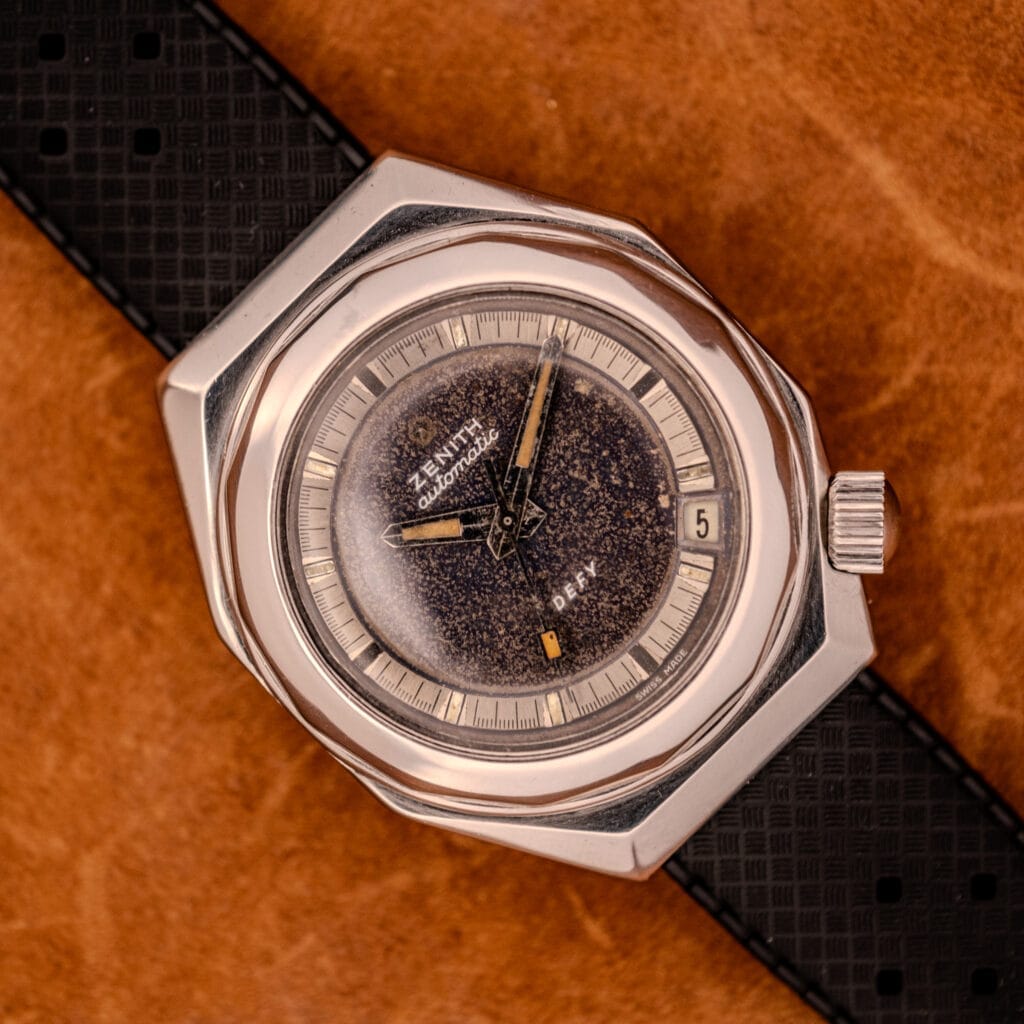 Zenith Automatic Defy NA.50.012.2 in stainless steel Cal. 2562 PC, featuring a speckled dial, date window, and black textured strap on brown leather.