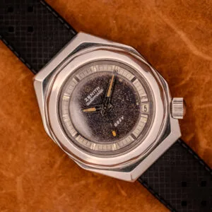 Zenith Automatic Defy NA.50.012.2 in stainless steel Cal. 2562 PC, featuring a speckled dial, date window, and black textured strap on brown leather.