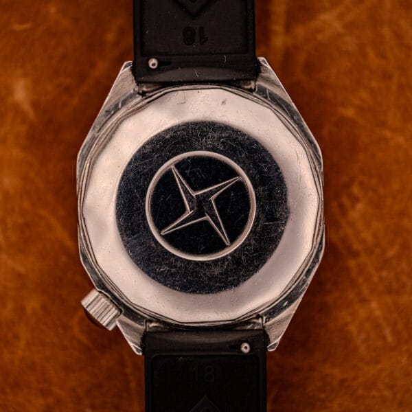 Back of a Zenith Automatic Defy NA.50.012.2 in stainless steel (Cal. 2562 PC), featuring a circular logo with a four-pointed star, shown on a brown leather surface.