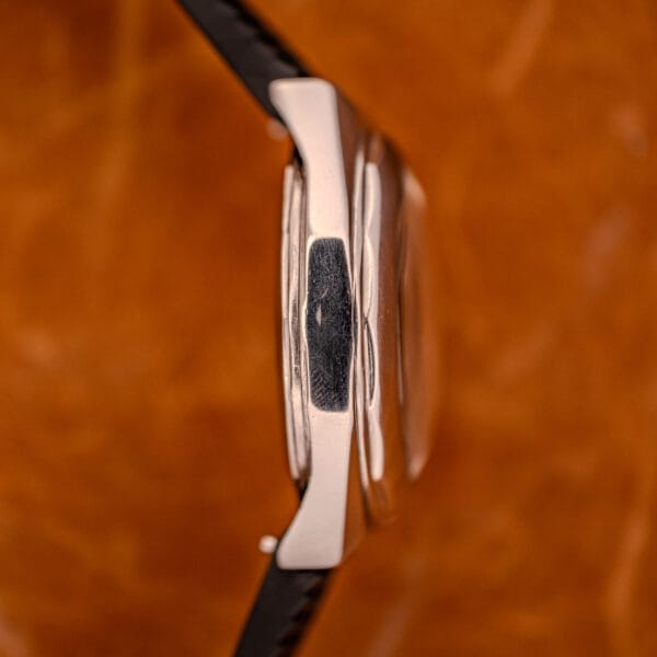 Side view of a Zenith Automatic Defy NA.50.012.2 in Stainless Steel Cal. 2562 PC wristwatch with black strap, displayed against a brown textured background.