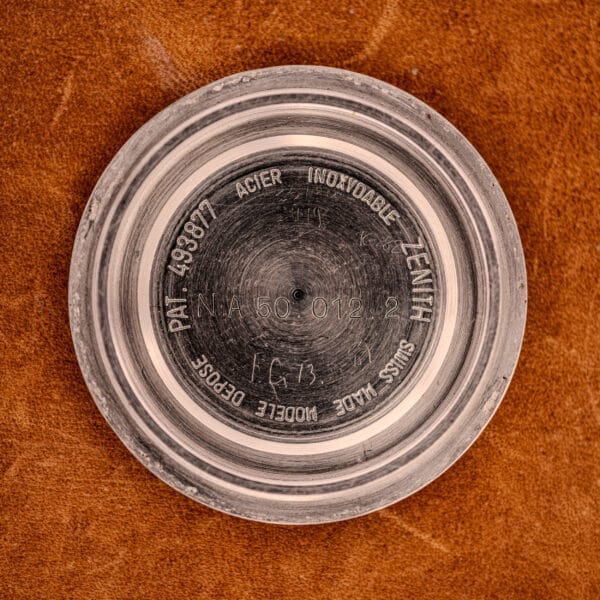 Close-up of a Zenith Automatic Defy NA.50.012.2 Stainless Steel Cal. 2562 PC watch case back, engraved with text, on a brown textured surface.
