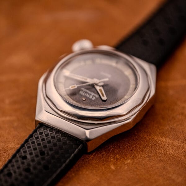 Close-up of a Zenith Automatic Defy NA.50.012.2 in Stainless Steel Cal. 2562 PC wristwatch with a black strap, displayed on a brown textured surface.