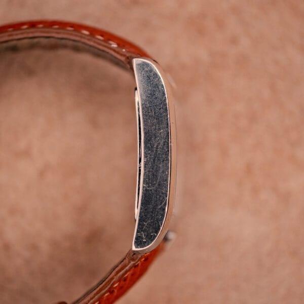 Close-up side view of a Baume Mercier Hampton MV045139 wristwatch with a copper dial and stainless steel case on a beige background.