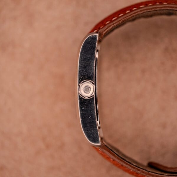 Close-up side view of a Baume Mercier Hampton MV045139 with a copper dial, stainless steel case, and brown leather strap on a light brown background.