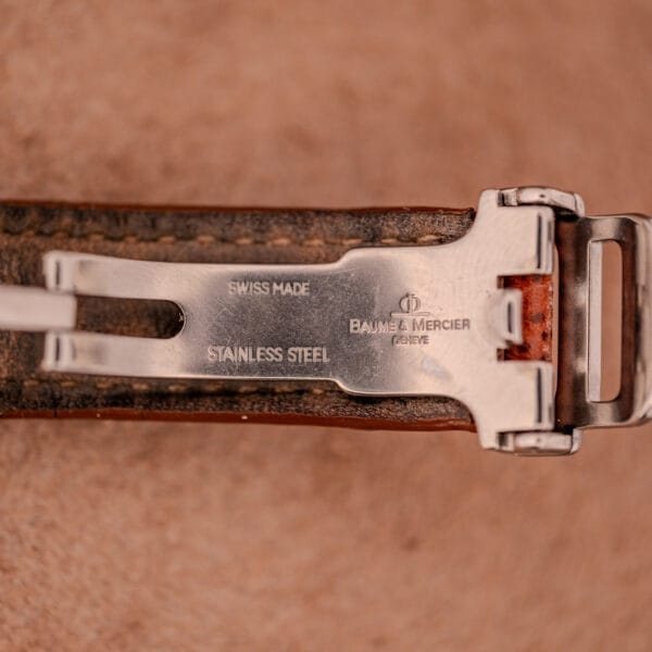 Close-up of the Baume Mercier Hampton MV045139 Stainless Steel clasp, engraved with "Swiss Made" and highlighting the refined craftsmanship of its copper dial design.