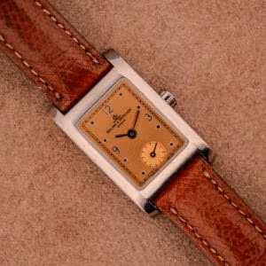 Baume & Mercier Hampton MV045139 angled wrist view showing copper salmon dial, polished steel rectangular case, and tobacco brown leather strap.