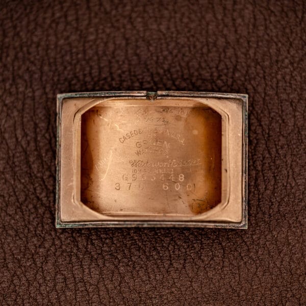 The Gruen Curvex Precision Ref. 370-600 features a 10k Gold Filled Case with engraved serial numbers on the inside back, showcased on a brown textured surface, emphasizing its timeless craftsmanship and precision.