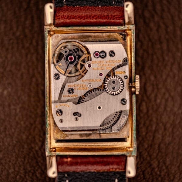 Close-up of a Gruen Curvex Precision Ref. 370-600 10k Gold Filled Case watch movement, featuring visible gears and text, set against a brown leather background for an elegant, intricate look.