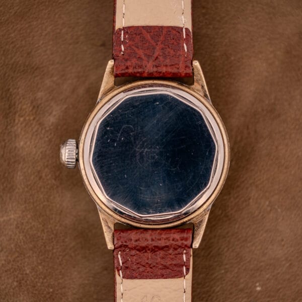 A Hamilton WWII Era U.S. Military Cal. 987S Hacking Seconds wristwatch with a scratched, faceted glass face and brown leather strap rests on a brown surface, highlighting its classic military design and hacking seconds feature.