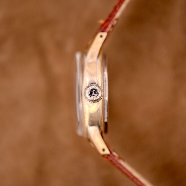 Side view of the Hamilton WWII Era U.S. Military Cal. 987S Hacking Seconds wristwatch with a brown leather strap, textured crown, and Cal. 987S movement, set against a brown background.