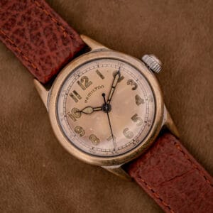 Hamilton WWII Era U.S. Military Cal. 987S Hacking Seconds wristwatch with a worn dial and brown leather strap, displayed on a brown background.