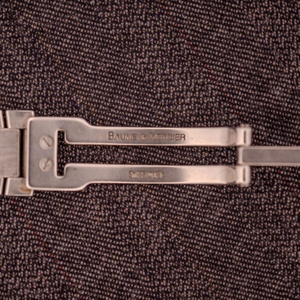 Close-up of a Baume Mercier Riviera Automatic MV045165 Guilloché Dial Swiss Made metal clasp on textured dark fabric, highlighting the watch’s refined elegance.