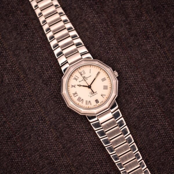 The Baume Mercier Riviera Automatic MV045165 with a silver Guilloché dial and Roman numerals rests on a brown textured fabric background.