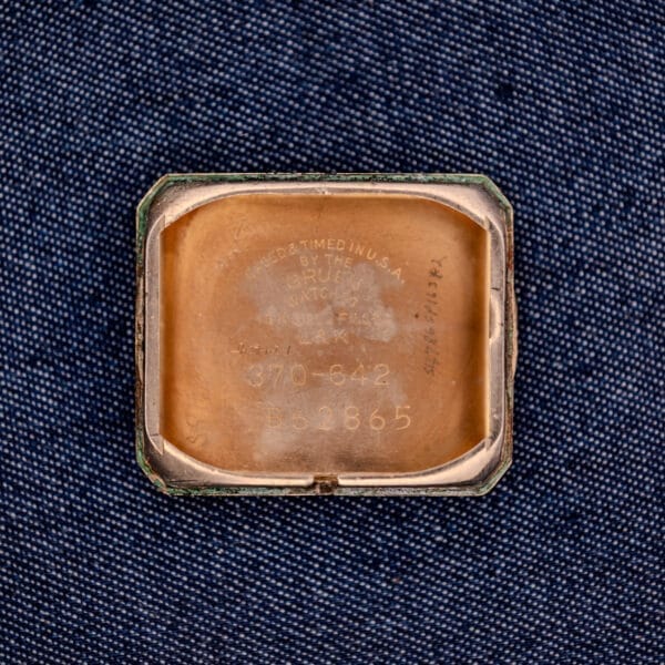 The inside case back of a Gruen Curvex Ref. 370-642 Art Deco "Pyramid" Crystal watch with engraved text, displayed on a blue textured fabric background.