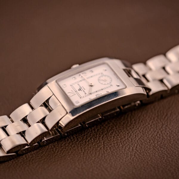 A Baume Mercier Hampton XL MV045063 with a white dial and stainless steel band, shown resting on a brown textured surface.