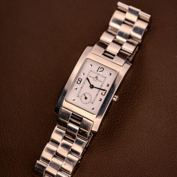 A Baume Mercier Hampton XL MV045063 with a white dial and stainless steel band rests elegantly on a brown textured surface.