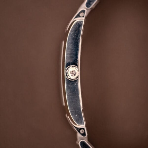 A close-up side view of the Baume Mercier Hampton XL MV045063 in stainless steel, featuring a textured crown and white dial, set against a brown background.