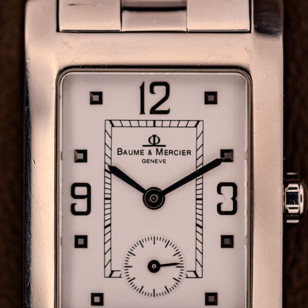 A close-up of the Baume Mercier Hampton XL MV045063 wristwatch features a white dial and stainless steel case, displaying the time as 1:48.