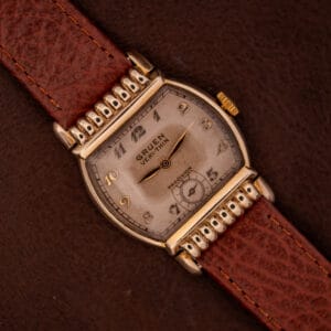 Gruen Veri-Thin Ref. 527/420 wristwatch with Art Deco hooded lugs and a brown leather strap displayed on a dark brown surface.