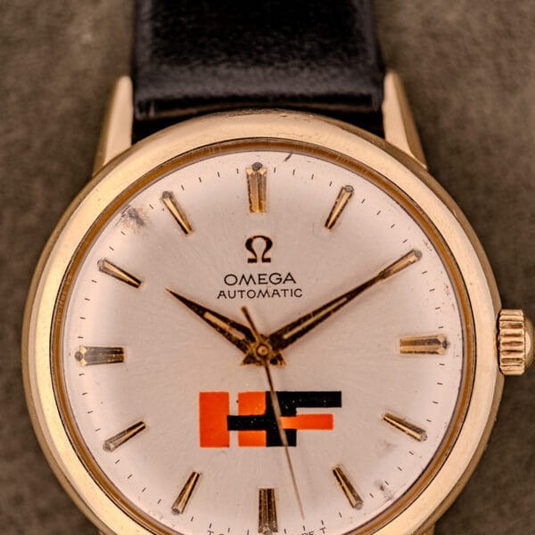 Close-up of an Omega Automatic Ref. LU 6304 wristwatch with "HF" logo dial, 10k gold-filled bezel, and black leather strap.