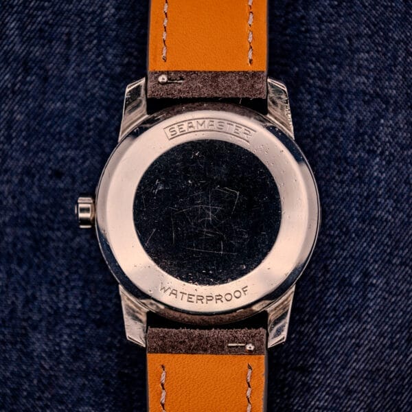 The Omega Automatic Seamaster 2846-2848 with a stainless steel sunburst dial and tan leather strap is displayed on a denim background.