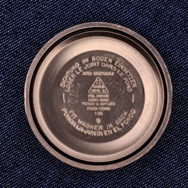 A stainless steel lid with multilingual instructions embossed inside, set on dark textured fabric, echoing the refined precision of the Omega Automatic Seamaster 2846-2848 Stainless Steel Sunburst Dial.