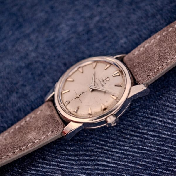 An Omega Automatic Seamaster 2846-2848 with a stainless steel case and sunburst dial, paired with a brown suede strap, rests on blue denim fabric.