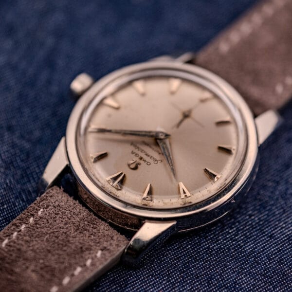 An Omega Automatic Seamaster 2846-2848 with a stainless steel case and sunburst dial, featuring a brown suede strap, displayed on blue denim fabric.