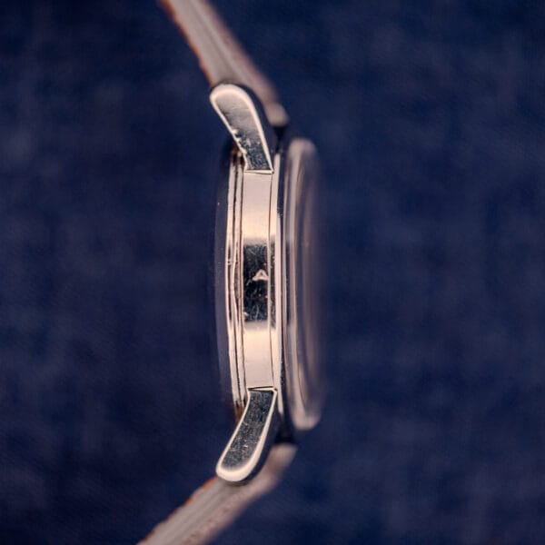 Side view of an Omega Automatic Seamaster 2846-2848 Stainless Steel with sunburst dial and leather strap, set against a blue textured background.