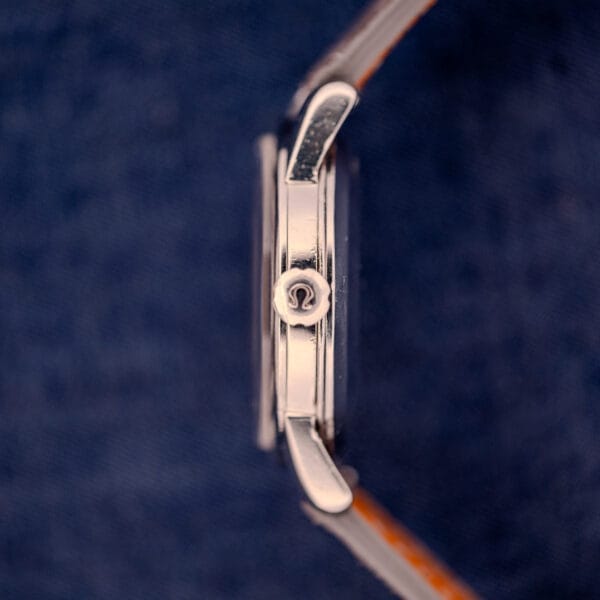 The Omega Automatic Seamaster 2846-2848 Stainless Steel Sunburst Dial wristwatch is captured in a side view, highlighting its crown against a dark blue fabric backdrop.