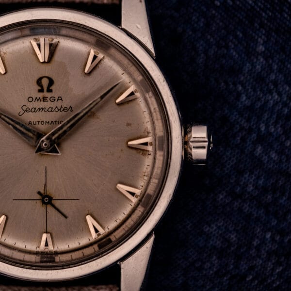 Close-up of an Omega Automatic Seamaster 2846-2848 with a stainless steel sunburst dial, set against a dark fabric background.