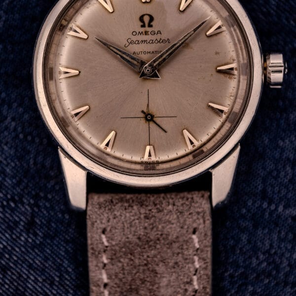 Close-up of an Omega Automatic Seamaster 2846-2848 with a stainless steel case, sunburst dial, and tan leather strap, resting on denim fabric.