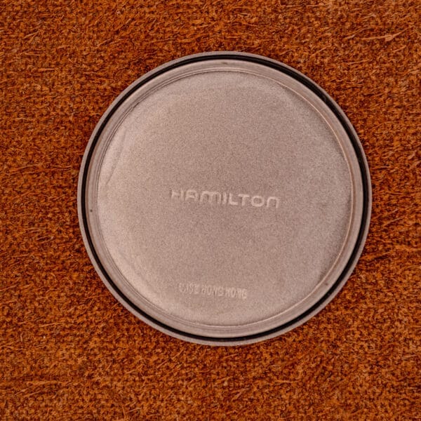 A Hamilton Khaki Ref. 9415A Black Dial Manual Wind Stainless Steel watch, featuring HAMILTON text and a black dial, lies on a textured brown surface.
