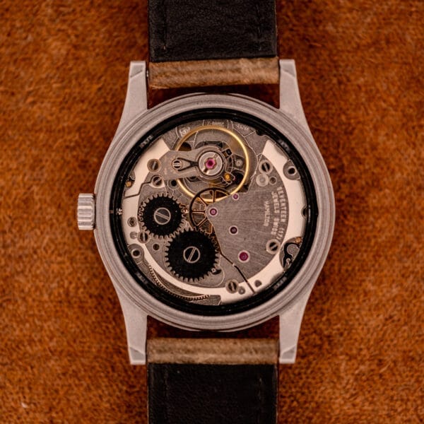 Close-up of a Hamilton Khaki Ref. 9415A Black Dial Manual Wind Stainless Steel wristwatch’s exposed mechanical movement, highlighting its gears and components on a brown textured surface.