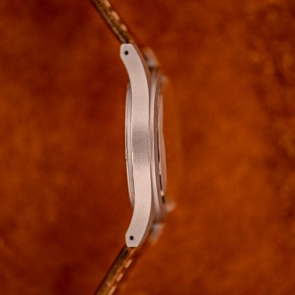 A close-up side view of the Hamilton Khaki Ref. 9415A with a black dial and manual wind stainless steel case, featuring a leather strap, set against a textured brown background.