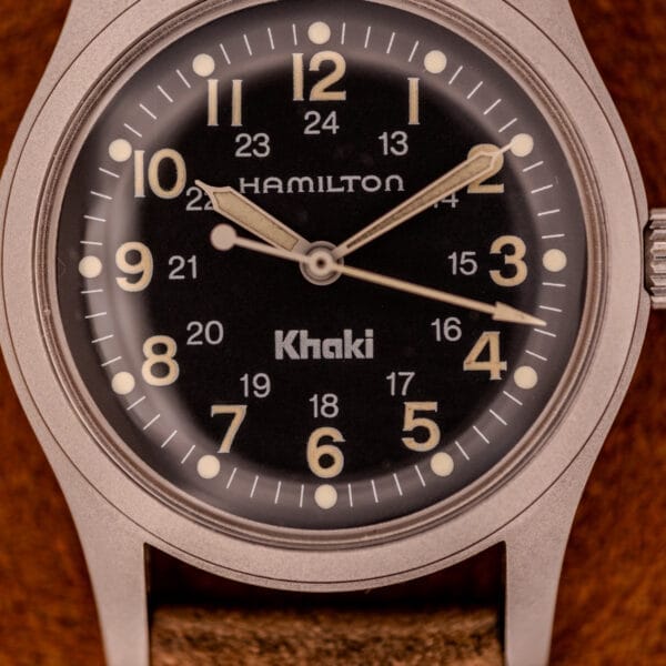 Close-up of the Hamilton Khaki Ref. 9415A Black Dial Manual Wind Stainless Steel wristwatch at 3:15, displaying a black dial with sharp white numerals.