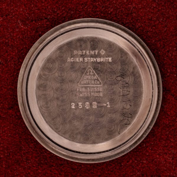 14k gold capped Omega Automatic Bumper Ref. 2582 with a silver case back engraved with the Omega logo and Cal. 351 details, displayed on a red textured background.