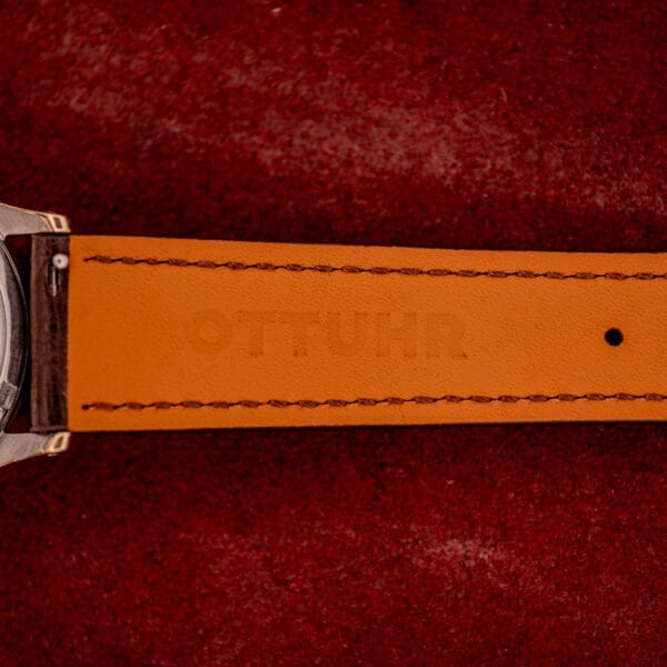 Close-up of an Omega Automatic Bumper Ref. 2582 14k Gold Capped Cal. 351 with a brown leather strap on red fabric embossed with OTTOUHR.