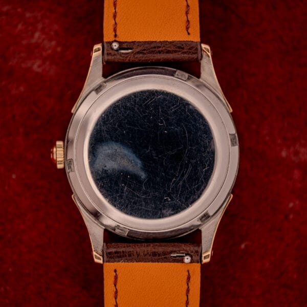 An Omega Automatic Bumper Ref. 2582 14k Gold Capped Cal. 351 with brown leather strap and a scratched caseback rests on a red textured background.