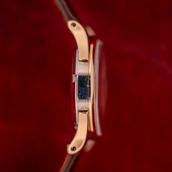 Side view of an Omega Automatic Bumper Ref. 2582 14k Gold Capped Cal. 351 wristwatch with a leather strap, shown against a red background.
