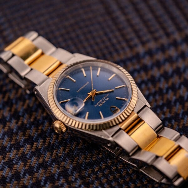 A Tudor Prince-Quartz Oysterdate Ref. 9150 with a two-tone blue dial rests on blue and brown textured fabric.