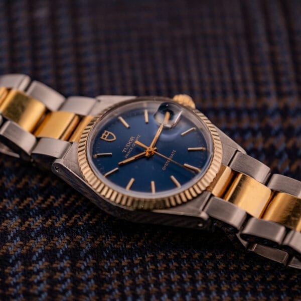 A Tudor Prince-Quartz Oysterdate Ref. 9150 Two-Tone Blue Dial wristwatch sits elegantly on brown and blue checkered fabric.