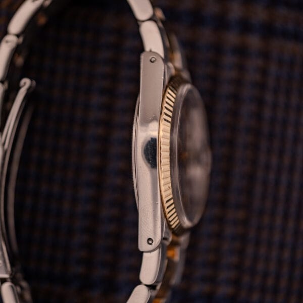 Side view of the Tudor Prince-Quartz Oysterdate Ref. 9150 Two-Tone Blue Dial wristwatch, featuring a metal band, gold ridged bezel, and vibrant blue dial, set against a dark textured background.