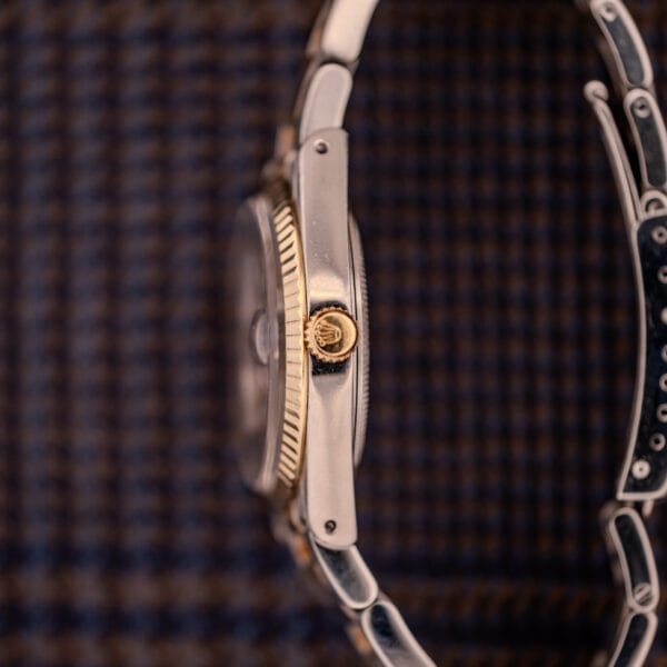 Side view of a Tudor Prince-Quartz Oysterdate Ref. 9150 Two-Tone Blue Dial wristwatch, featuring a textured crown and metal bracelet, set against a checkered background.