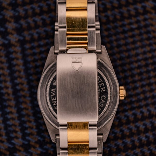 Close-up of the Tudor Prince-Quartz Oysterdate Ref. 9150 Two-Tone Blue Dial, highlighting its metal bracelet and case back against a patterned fabric background.