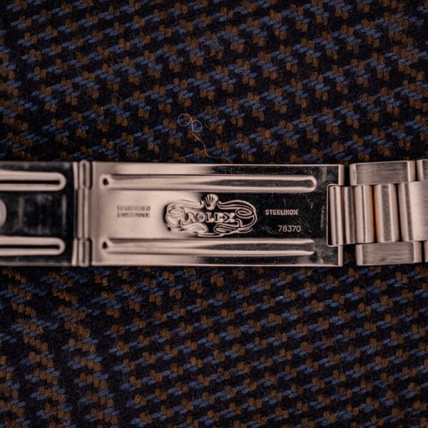 Close-up of a Tudor Prince-Quartz Oysterdate Ref. 9150 clasp with engravings, set against textured brown and blue fabric—a refined pairing that highlights the elegance of this two-tone blue dial timepiece.