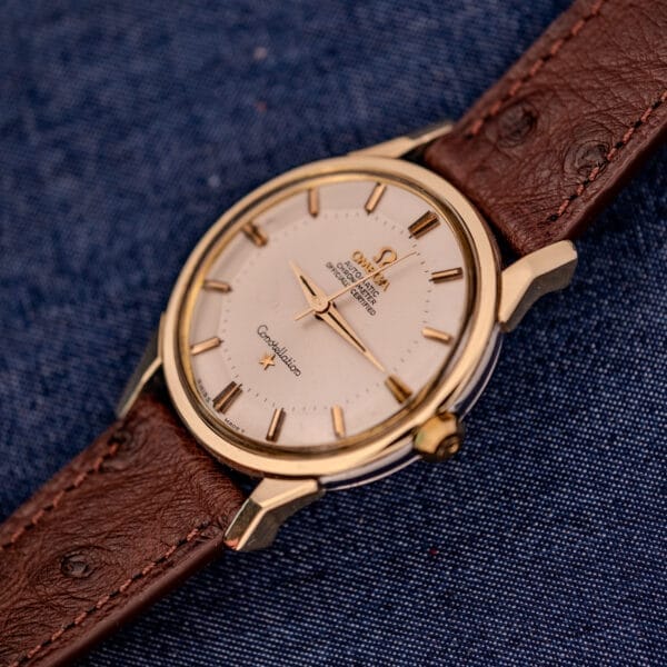 Omega Constellation Pie-Pan Dial Ref. 167.005 14k gold capped wristwatch with a brown leather band is displayed on blue fabric, showcasing its distinctive design.